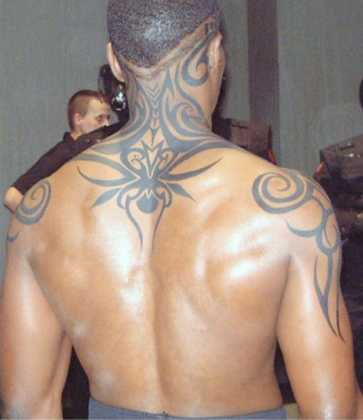 the back of a man with tattoos on his upper and lower body, standing in front of other men