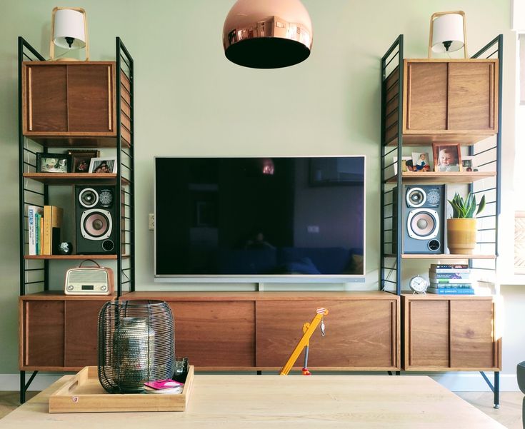 a flat screen tv sitting on top of a wooden shelf in front of a wall mounted speaker