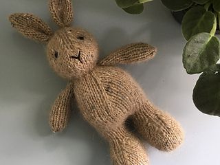 a knitted bunny sitting next to a potted plant on a white table top