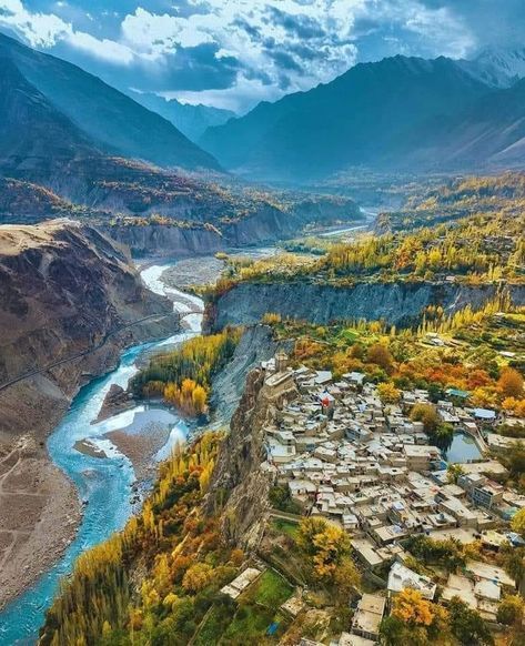 an aerial view of a valley and river in the middle of mountains with houses on each side