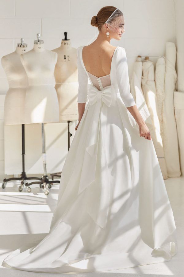 a woman standing in front of mannequins wearing a white dress with long sleeves