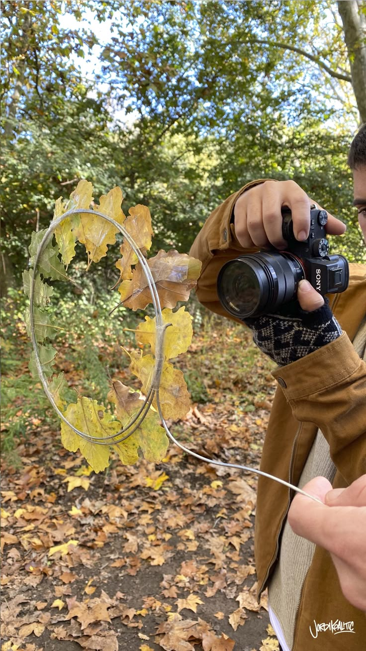 a man holding a camera and taking a photo in the woods with leaves on the ground