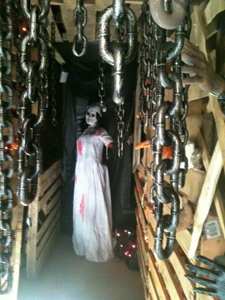 a person dressed as a ghost in a storage area with chains hanging from the ceiling