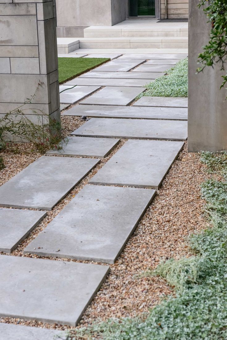 a stone walkway in front of a building with grass growing on the ground and bushes