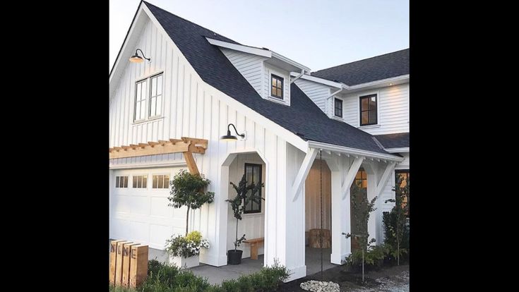 a white house with black shingles and two story windows on the front door is surrounded by greenery