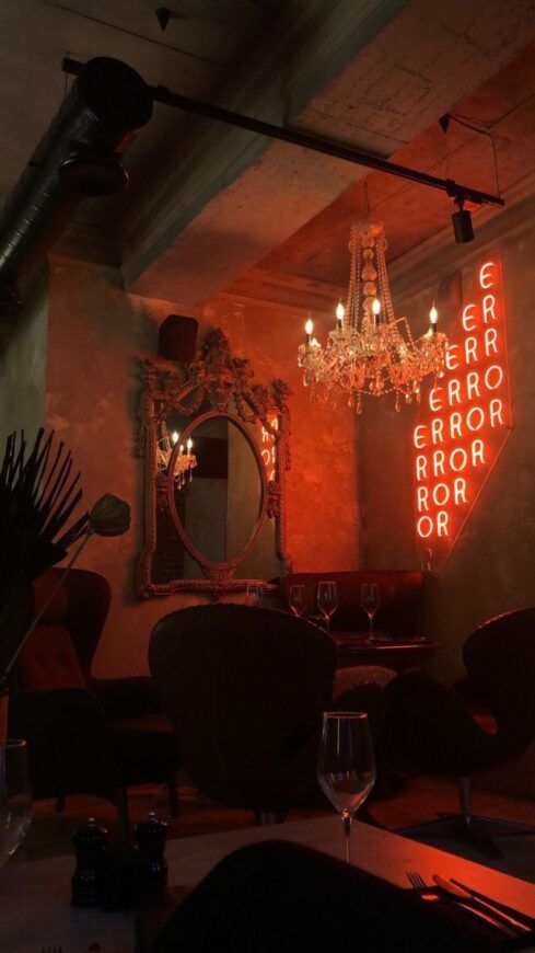 a dimly lit room with chandelier, mirror and wine glasses on the table