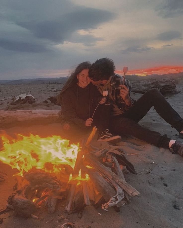 two people sitting around a campfire at sunset