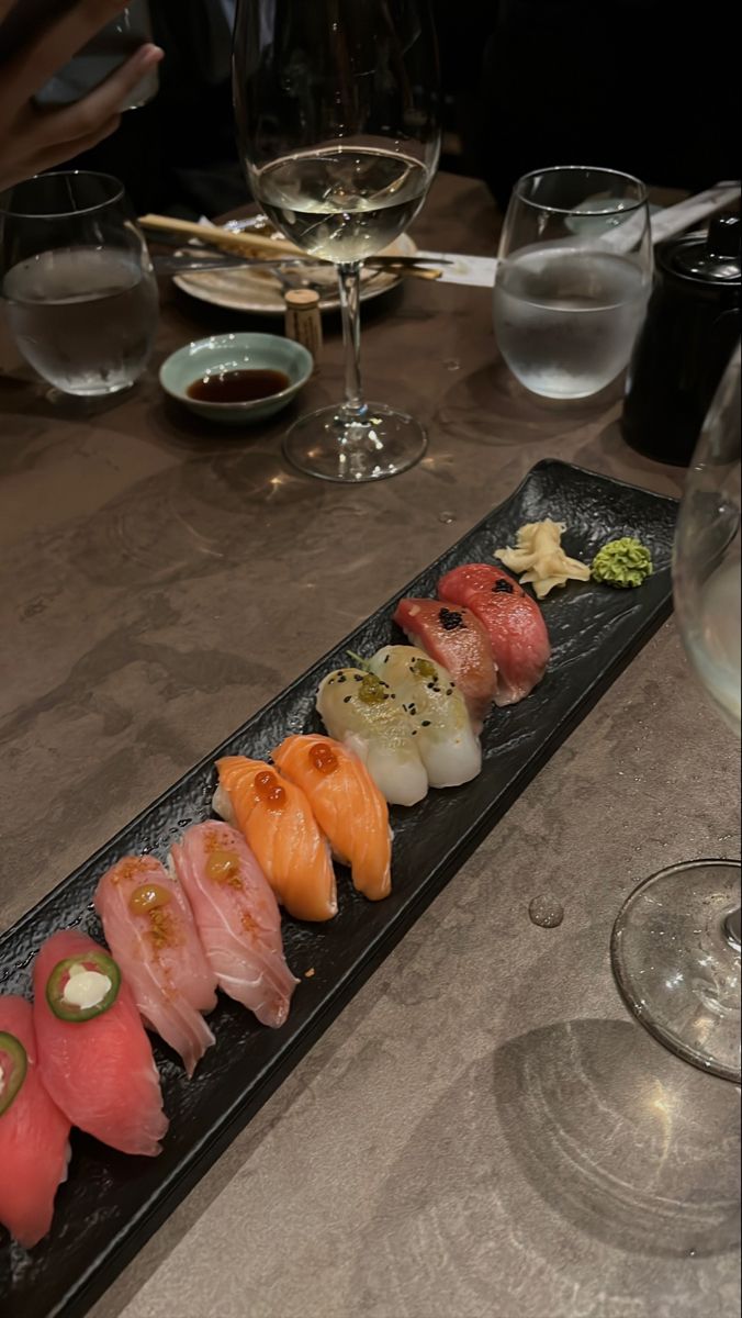 a long black plate with sushi on it next to some wine glasses and water