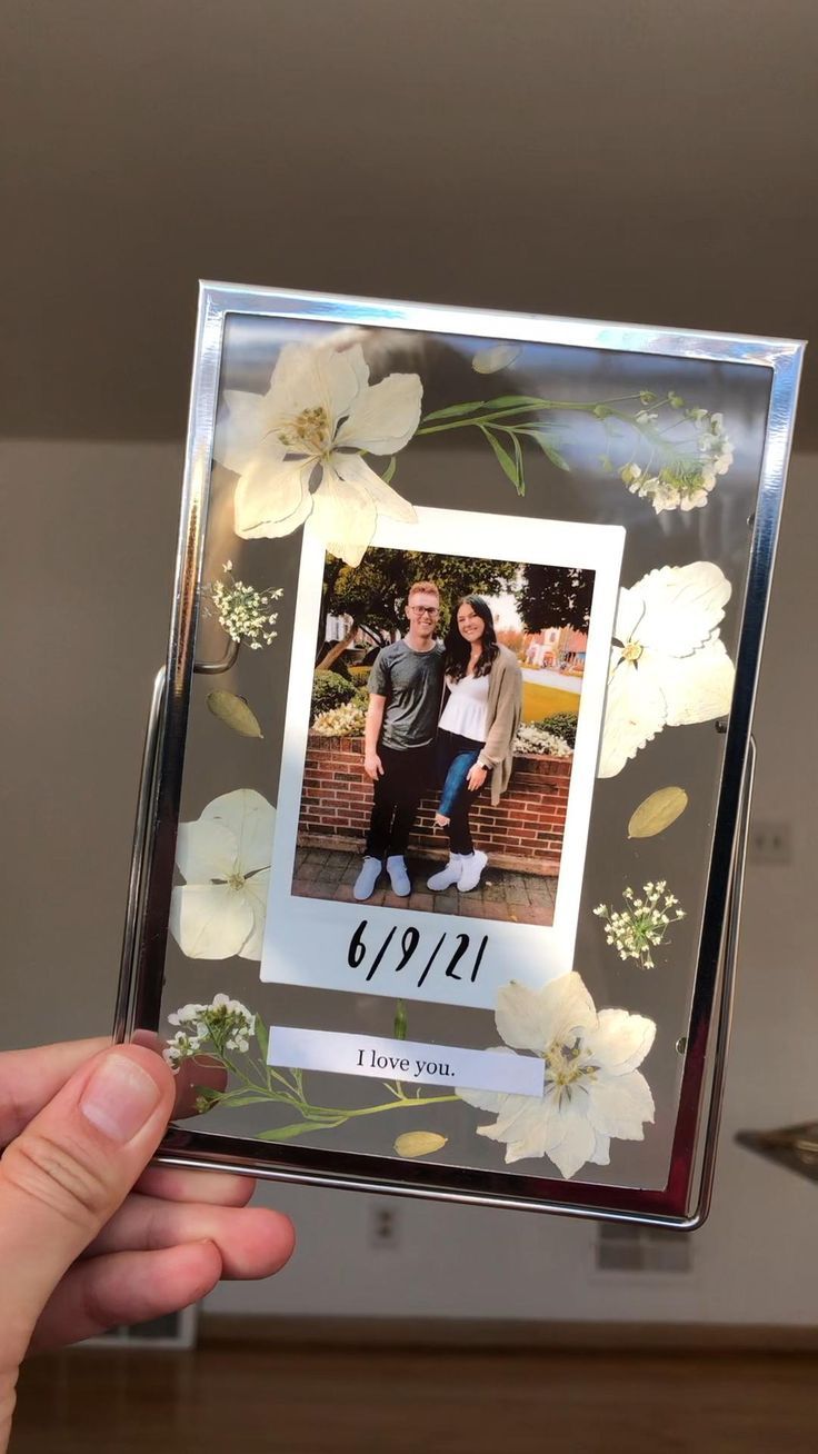 a person holding up a photo frame with white flowers on the front and bottom side