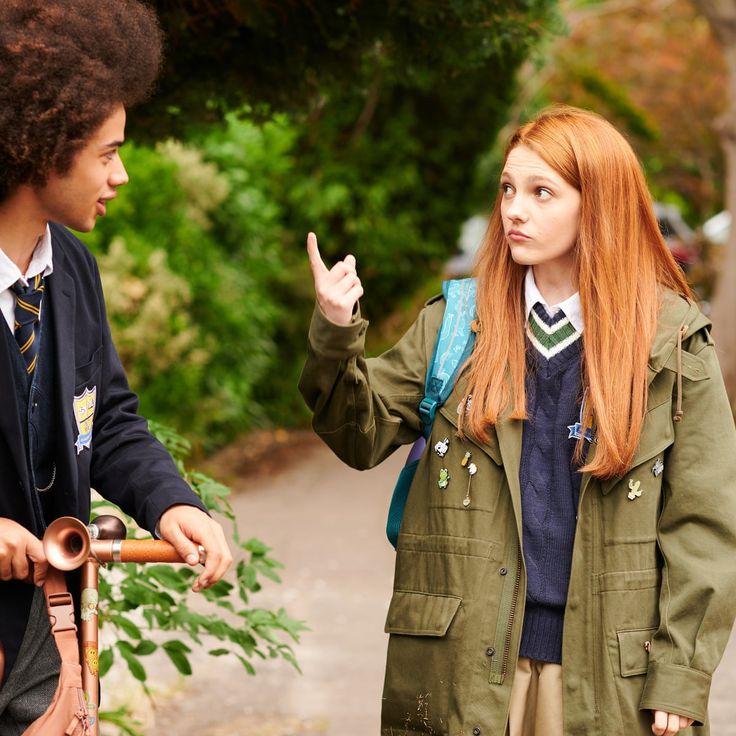 two young people standing next to each other on a sidewalk with trees in the background