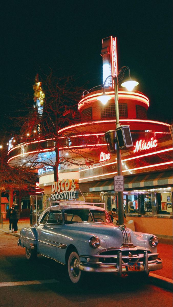 an old car parked in front of a movie theater