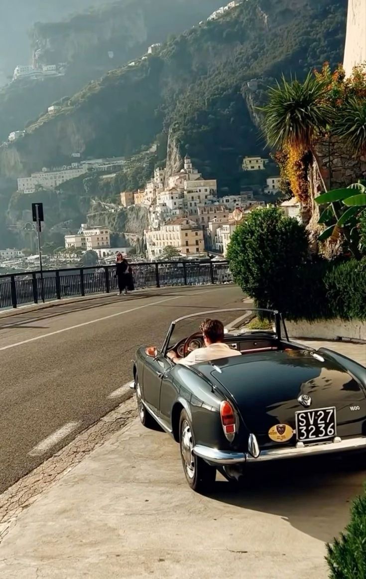 a car parked on the side of a road next to a hill with buildings in the background