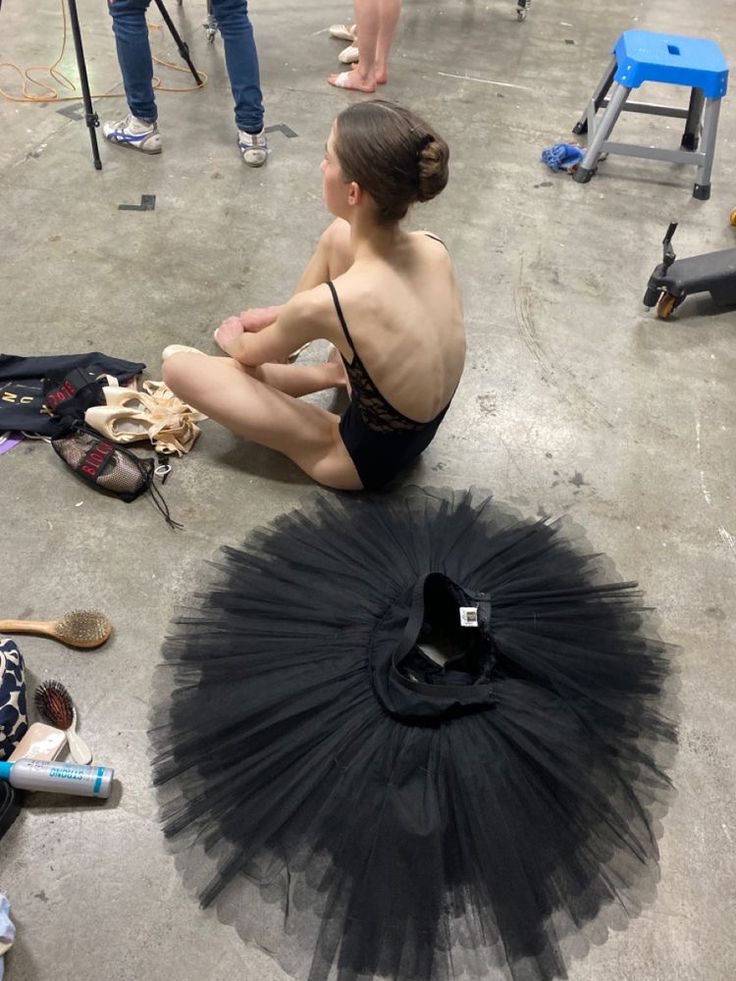 a woman sitting on the floor in front of a black tutu skirt and shoes