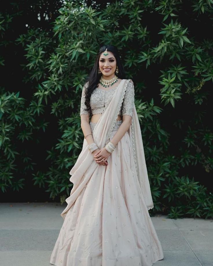 a woman in a pink lehenga standing on the sidewalk with greenery behind her