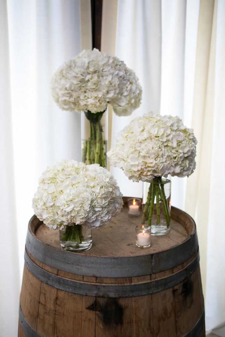 three vases filled with white flowers sitting on top of a barrel next to candles