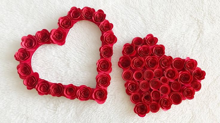 two hearts made out of rolled up red paper roses sitting next to each other on a white surface