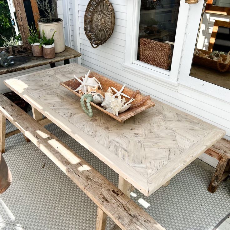 a wooden table sitting on top of a patio next to a white house with a potted plant