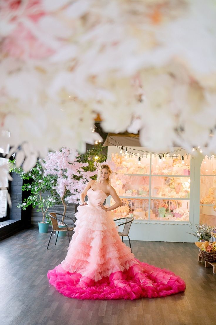 a woman in a pink dress standing on a wooden floor next to flowers and lights