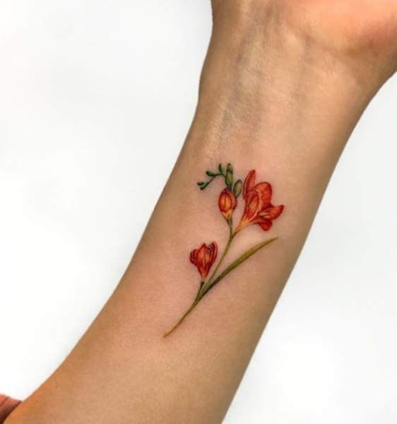 a woman's wrist tattoo with red flowers on the left side of her arm