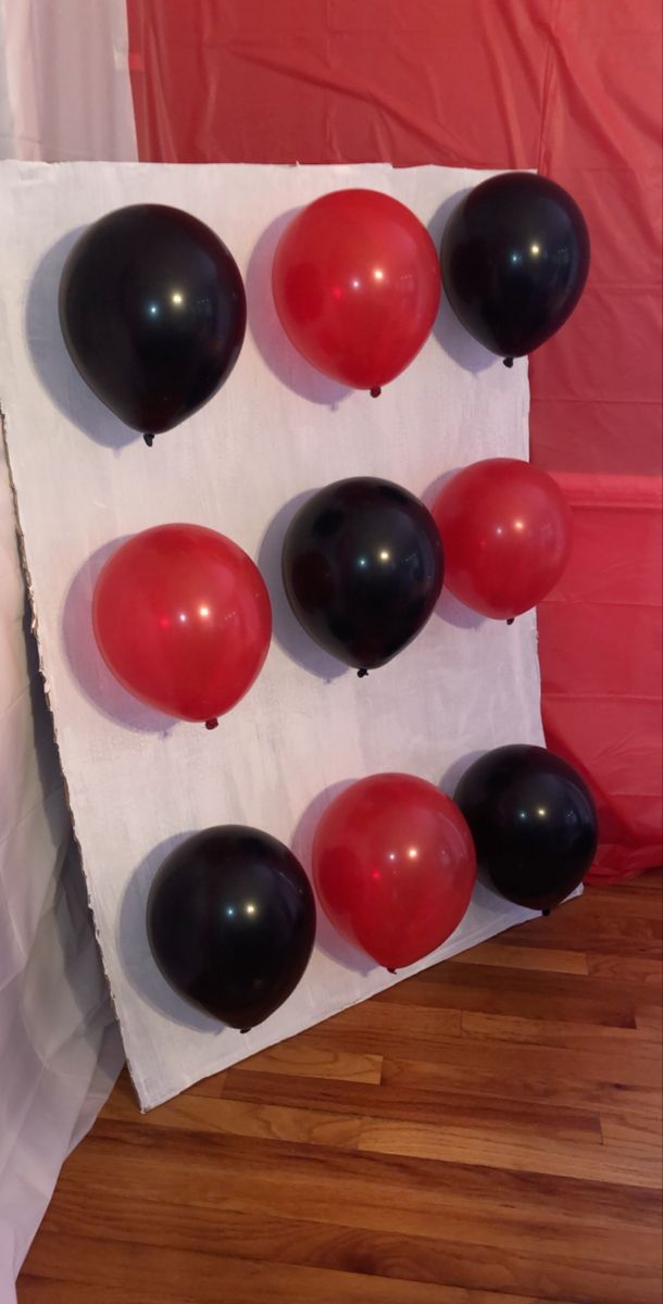 black and red balloons are arranged on a white sheet in front of a red wall