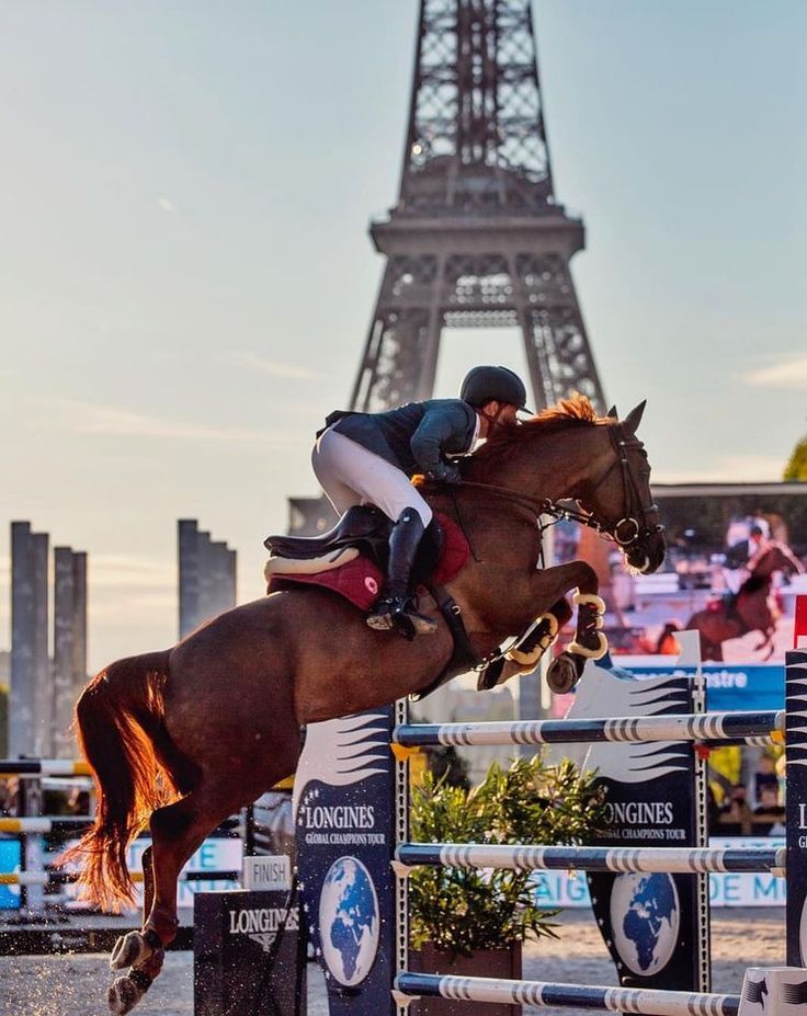 a horse and rider jumping over an obstacle in front of the eiffel tower