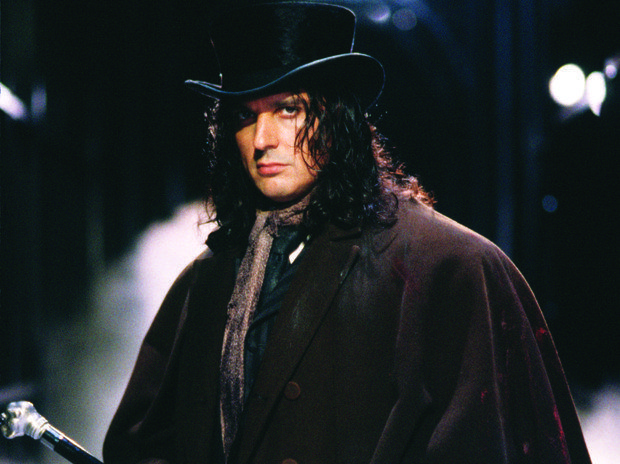 a man with long hair wearing a black top hat and holding a cane in his hand