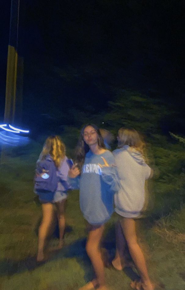 three girls are standing in the grass near a street light at night with their arms around each other