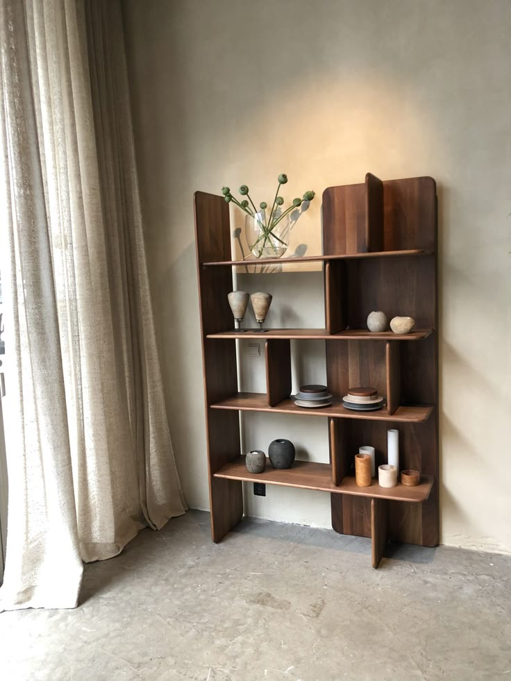 a wooden shelf with vases and other items on it in front of a window