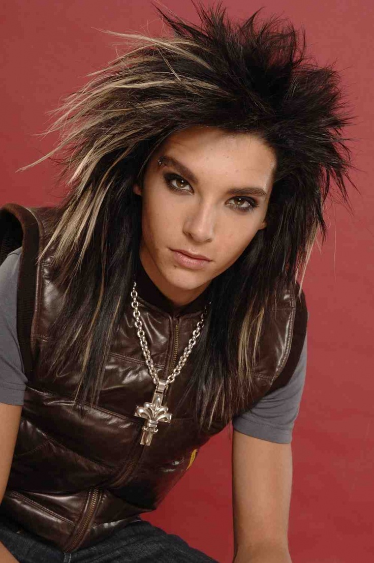 a young woman with long hair wearing a leather vest and necklace, posing in front of a red background