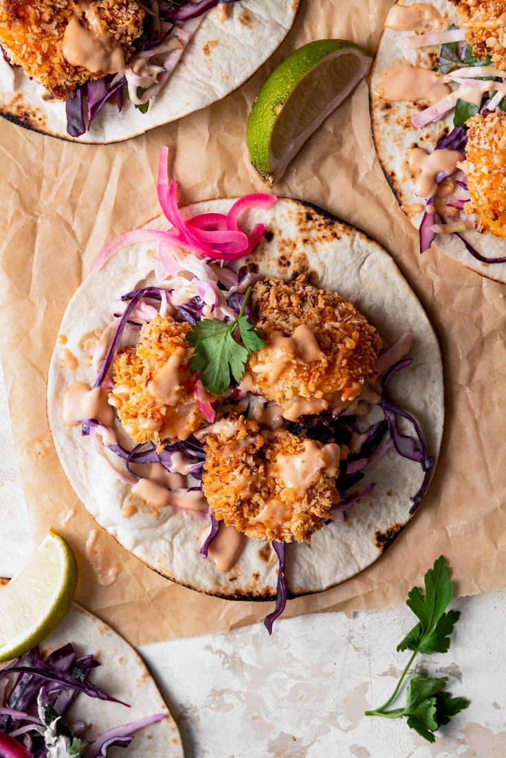 two fish tacos on tortillas with cole slaw and lime wedges