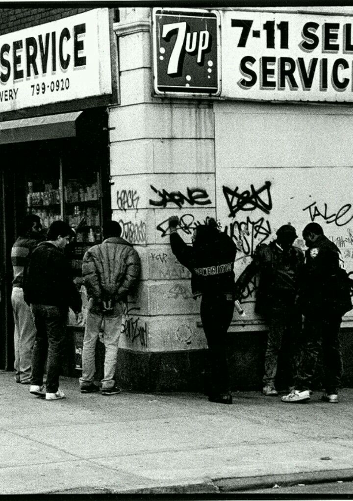 black and white photograph of people standing in front of a store with graffiti on the wall