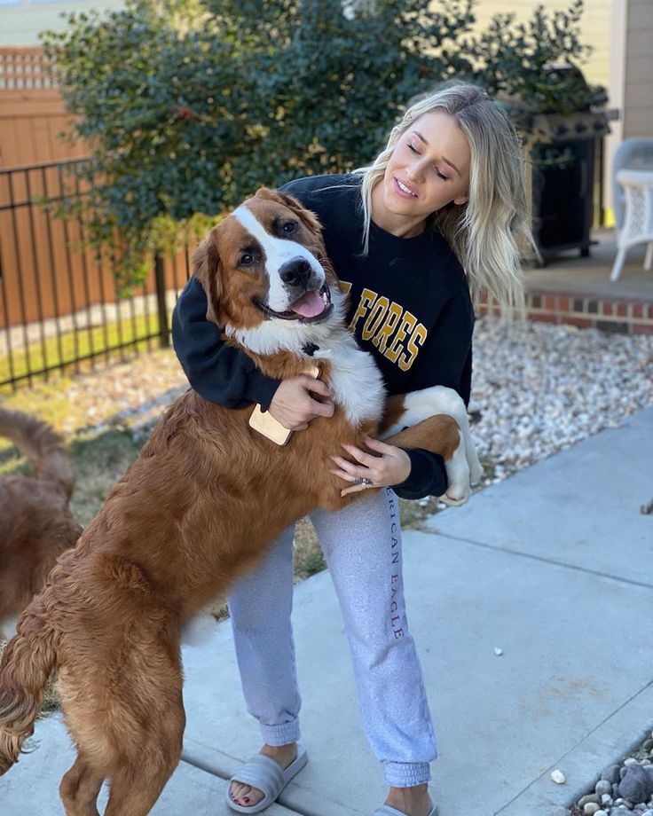 a woman holding two dogs in her arms on the sidewalk with another dog behind her