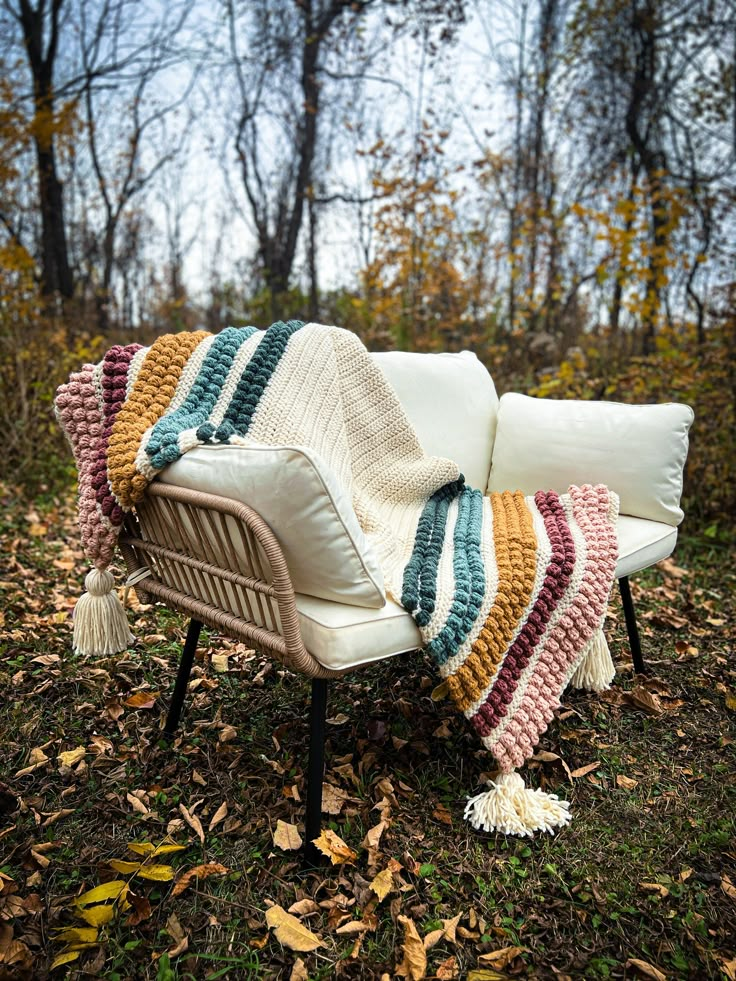 a white chair with a crocheted blanket on it sitting in the grass next to some leaves