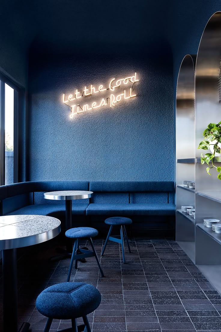 the interior of a restaurant with blue walls and tables, stools, and potted plant