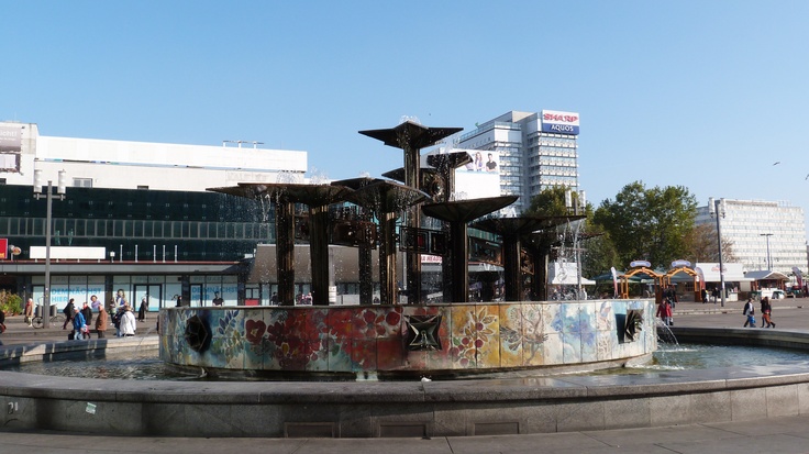 a fountain with lots of graffiti on it in the middle of a city square surrounded by tall buildings