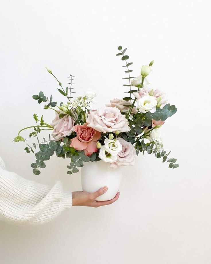 a person holding a white vase filled with flowers