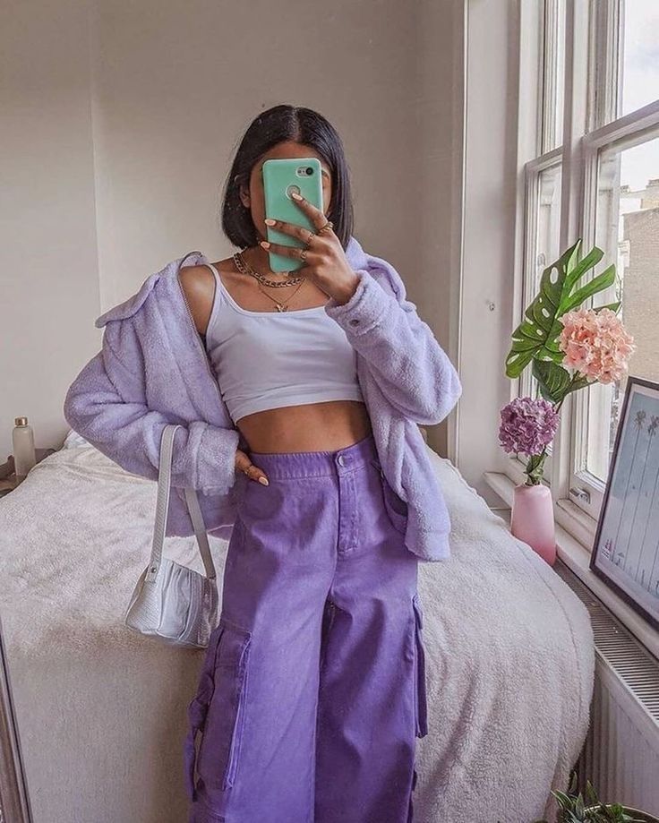 a woman taking a selfie while wearing purple pants and a white cropped top