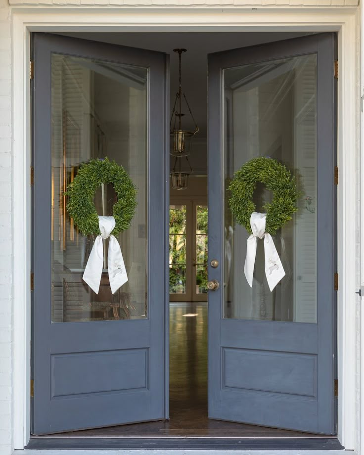 two wreaths on the front doors of a house