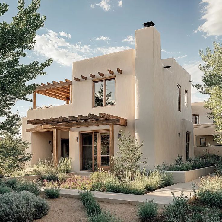 an adobe style house in the desert surrounded by trees and shrubs, with a pergolated walkway leading to the front door