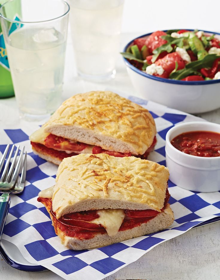 two sandwiches sitting on top of a blue and white checkered napkin next to a bowl of salad