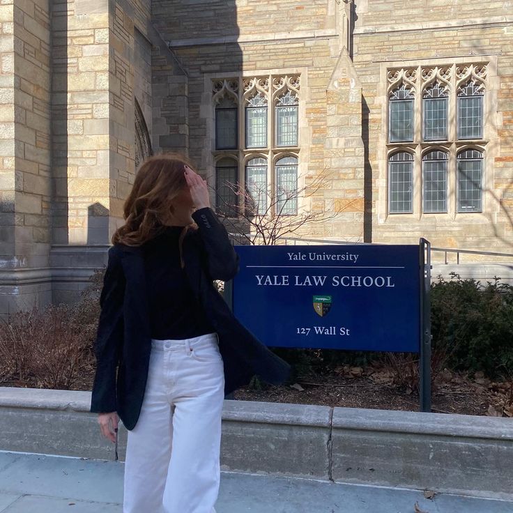 a woman is standing in front of the yale law school sign and looking up into the sky