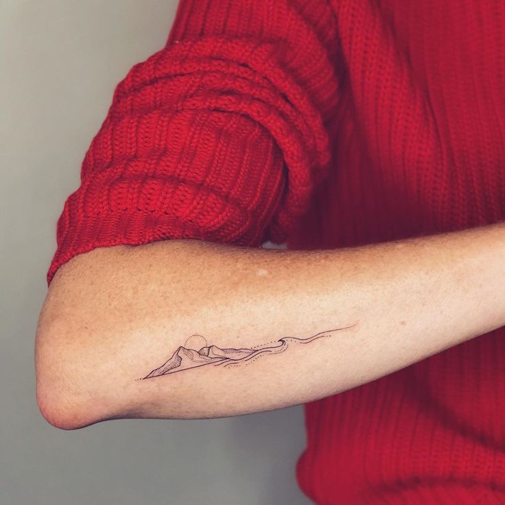 a woman's arm with a small mountain tattoo on the left side of her arm