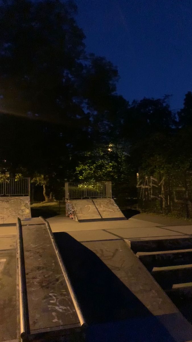 a skateboard park at night with ramps and steps lit up by street lights in the background