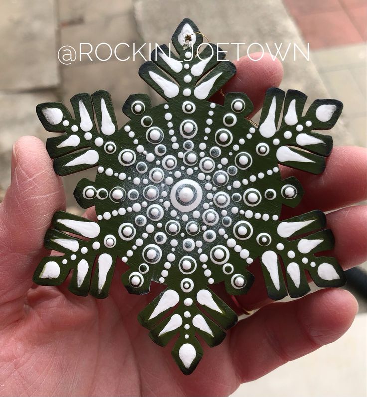 a hand holding a green and white snowflake ornament