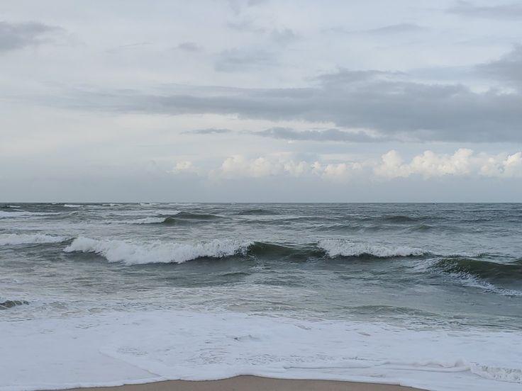 an ocean view with waves crashing on the shore and clouds in the sky above it