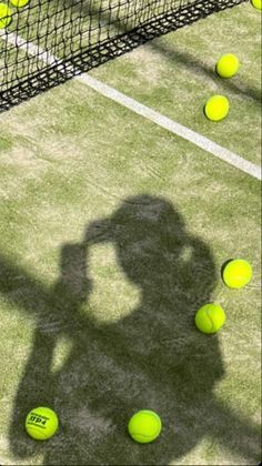 a shadow of a person standing on a tennis court with balls in front of him