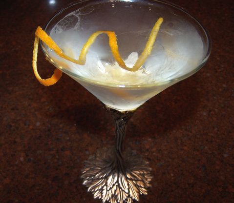 a martini glass with an orange peel garnish on the rim and ice in it