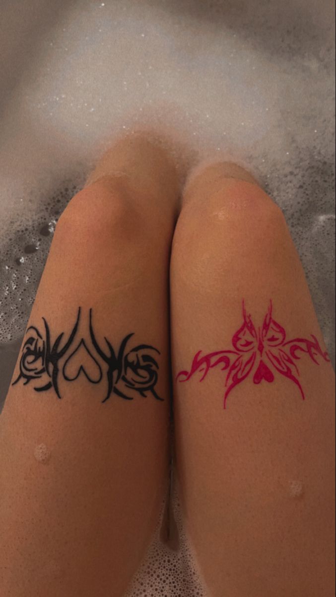 two women with tattoos on their legs sitting in a bathtub filled with water and bubbles