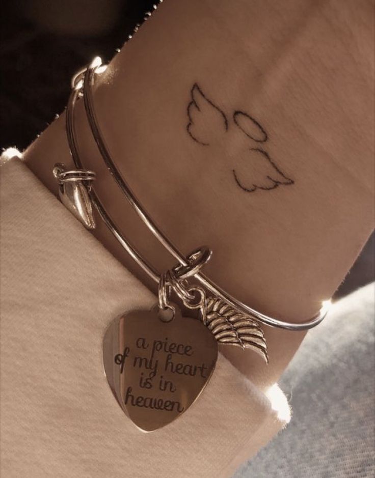 a close up of a person's wrist with a heart and an angel charm on it