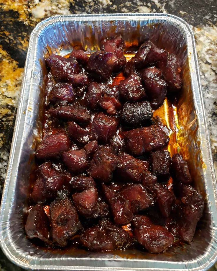 a tin pan filled with meat sitting on top of a granite counter next to a knife